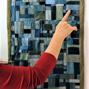 Pode incluir: Uma tape&ccedil;aria de parede feita de tecido de ganga em v&aacute;rios tons de azul e verde. O tecido &eacute; cortado em quadrados e ret&acirc;ngulos e costurado para criar um design de patchwork. A tape&ccedil;aria de parede &eacute; emoldurada com uma borda de tecido marrom.