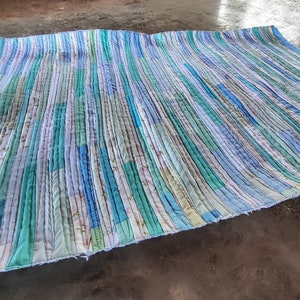 Puede incluir: Una colcha hecha a mano con un patr&oacute;n a rayas en tonos azules y verdes. La colcha est&aacute; hecha de retazos de tela y tiene un aspecto r&uacute;stico y vintage.