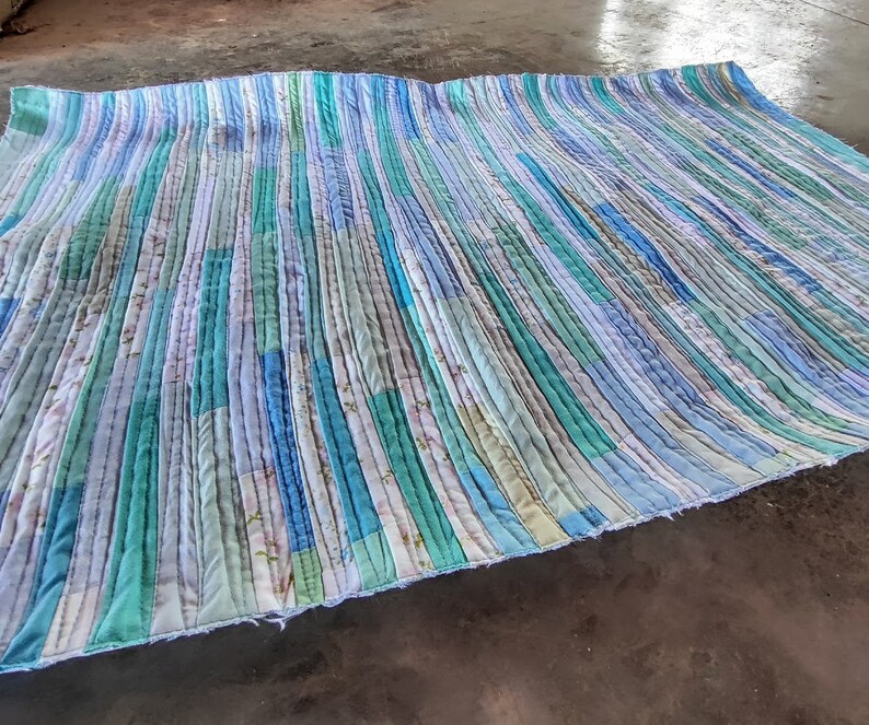 Puede incluir: Una colcha hecha a mano con un patr&oacute;n a rayas en tonos azules y verdes. La colcha est&aacute; hecha de retazos de tela y tiene un aspecto r&uacute;stico y vintage.