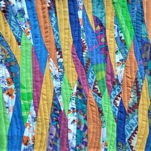 Może przedstawiać: Zbliżenie kolorowej kołdry z patchworkowym wzorem. Kołdra posiada pionowe paski w r&oacute;żnych kolorach, w tym ż&oacute;łtym, niebieskim, pomarańczowym, zielonym i fioletowym. Paski są zszyte widocznymi szwami.