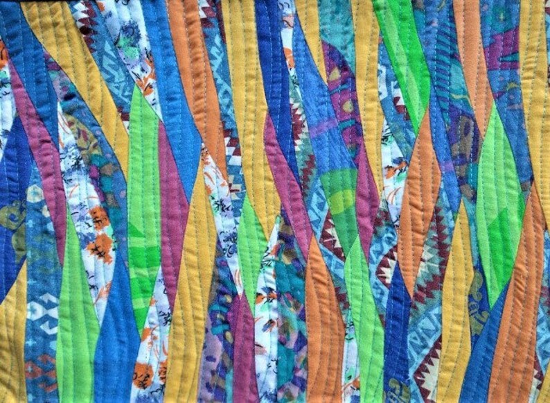 Może przedstawiać: Zbliżenie kolorowej kołdry z patchworkowym wzorem. Kołdra posiada pionowe paski w r&oacute;żnych kolorach, w tym ż&oacute;łtym, niebieskim, pomarańczowym, zielonym i fioletowym. Paski są zszyte widocznymi szwami.