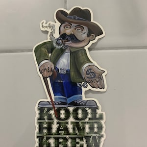 May include: A cartoon sticker of a man wearing a brown cowboy hat, green plaid shirt, blue jeans, and brown boots. He is holding a walking stick and has a cigar in his mouth. The sticker says "Kool Hand Krew" in green and black plaid.