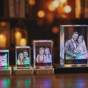 May include: A collection of personalized photo gifts. The images are encased in clear glass blocks, each illuminated with colorful LED lights. The photos include a cat, a couple, and a pair of children. The largest block features a wedding photo.