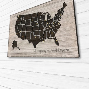 May include: A wooden map of the United States with gold heart-shaped push pins marking locations. The map has a distressed wood background and the text "Life is a journey best traveled together" is printed below the map.