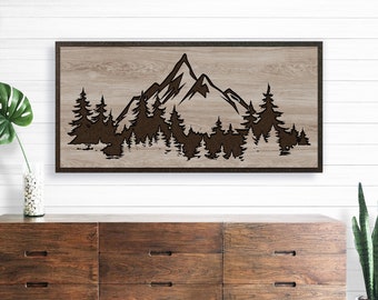 May include: A wood wall art piece with a brown mountain and forest silhouette design. The design is cut out of the wood, creating a 3D effect.