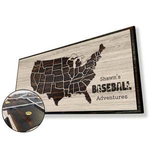 May include: A wooden sign with a map of the United States, with the states outlined in dark brown. The sign has the text "Shawn's Baseball Adventures" in dark brown letters.