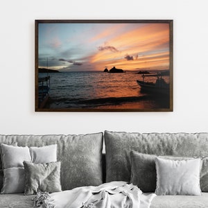 May include: A scenic sunset over the ocean with two boats silhouetted in the foreground. The sky is a vibrant mix of orange, pink, and blue with wispy clouds.