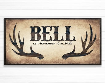May include: A rustic wooden sign with a brown background and black antlers on either side. The sign says "BELL EST. SEPTEMBER 10TH, 2022".