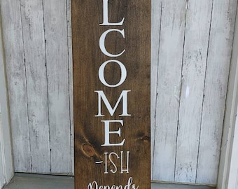 May include: A wooden sign with the word "WELCOME" written vertically in white paint. Below the word, it reads "ish Depends On Who You Are."