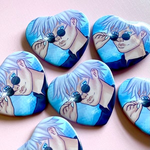 May include: Five heart-shaped buttons with a blue and white background. Each button features a cartoon illustration of a person with white hair, wearing sunglasses and a black shirt. The text "Taylor Seldom 2021" is printed on each button.