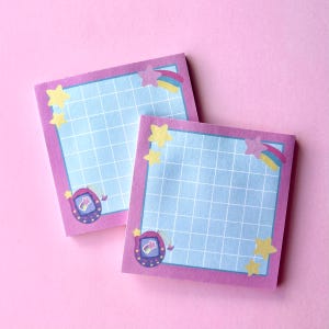 May include: Two square sticky notes with a light blue grid pattern and a pink border. Each note features a cartoon shooting star, yellow stars, and a retro handheld game design. The background is a solid pink.