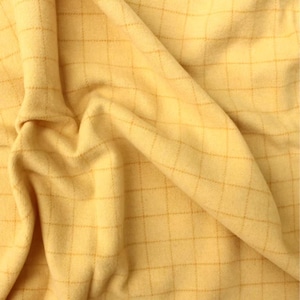 May include: Close-up of a soft, yellow fabric with a grid pattern. The fabric is draped, showing folds and texture. The grid lines are a slightly darker shade of yellow, creating a subtle contrast. The overall appearance is warm and inviting.