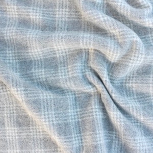 May include: A close-up of a soft, gray and white plaid fabric. The fabric is woven with a subtle texture and has a slightly fuzzy appearance.