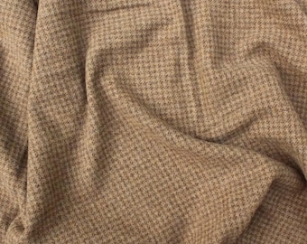 Può includere: Primo piano di un tessuto beige con un piccolo motivo a pied-de-poule ripetuto. Il tessuto è drappeggiato, creando pieghe e ombre morbide. La trama sembra morbida e possibilmente tessuta, adatta all'abbigliamento o all'arredamento.
