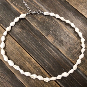 May include: A white seashell necklace with a silver clasp. The necklace is made of small, white seashells strung together on a silver chain.
