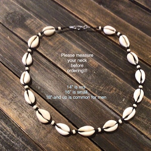 May include: A necklace made of cream-colored seashells strung on a black cord. The necklace is displayed on a wooden surface. Text on the image reads: "Please measure your neck before ordering!!!" and sizing information.
