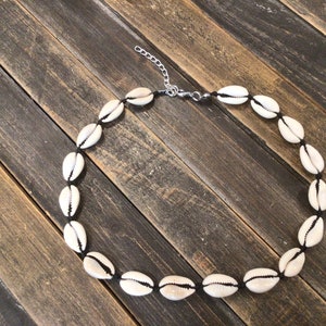 May include: A white shell necklace with black string and a silver clasp. The necklace is on a wooden surface.