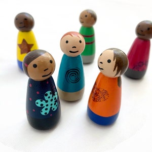 May include: Set of six hand-painted wooden peg dolls. The dolls are all different colors and have unique designs. The dolls are standing on a white surface.