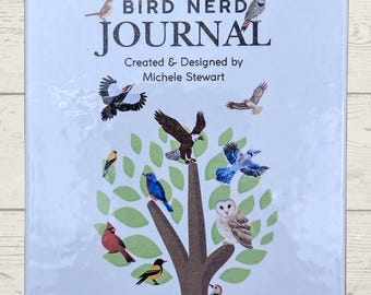 Puede incluir: Un diario « A Simple Bird Nerd » con una cubierta azul claro. El diario presenta una ilustración de un árbol con varios pájaros coloridos. El título está en letras negras grandes, con el nombre del diseñador debajo. El diario está encuadernado en espiral en la parte superior.