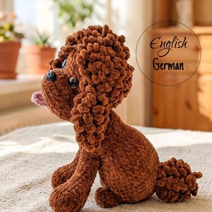 May include: A brown crocheted dog plush toy with a textured, curly yarn finish, large black plastic eyes, a small black nose, and a light pink tongue sticking out. The text "English German" is visible in a circle on the right side of the image.