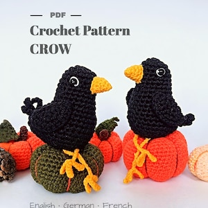 Pode incluir: Um padrão de crochê em PDF para um corvo, com dois pássaros pretos de crochê com bicos e olhos laranja, cada um empoleirado em uma pequena abóbora de crochê laranja ou verde-oliva. O texto diz PDF Crochet Pattern CROW e English · German · French.