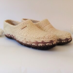 One pairs of beige wool slippers with brown and pink trim. The slippers have a crocheted texture and a label that says 'Handmade'.