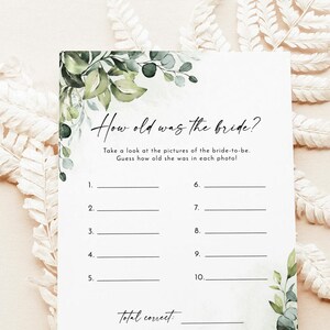 May include: A white card with the text "How old was the bride?" and fill-in-the-blank lines for a bridal shower game. The card is decorated with green foliage and a floral design. The card is surrounded by decorative elements.