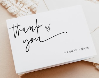 May include: White thank you card with black calligraphy that says "thank you" with a small heart drawn next to the word "thank". The card has the names "HANNAH + DAVE" printed in black at the bottom.