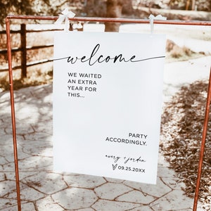 May include: A white sign with black text on a copper stand. The sign reads "welcome we waited an extra year for this... party accordingly. avery + jorden 09.25.20XX".