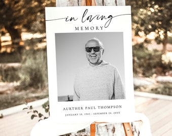 May include: A black and white photo of a man wearing sunglasses is on a white sign with the text "in loving memory" at the top. The sign also includes the text "Aurther Paul Thompson, January 10, 1945 - September 24, 20XX". The sign is on an easel.