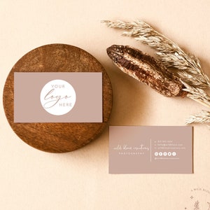 May include: A light brown business card with the text "wild bloom creators photography" and contact information. The card is on a beige background with a dried grass stalk and a wooden coaster with a second business card that says "YOUR LOGO HERE" in a circle.
