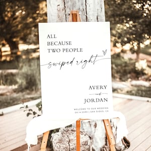 May include: A white wedding sign with black text that reads "All because two people swiped right." The sign also includes the names Avery and Jordan, the wedding date 08.14.20XX, and the location San Diego, CA.