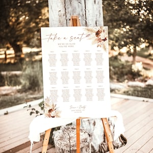 May include: A white wedding seating chart with a floral design and the text "Take a seat, we're so glad you're here." The chart lists tables and guest names. The bottom of the chart says "Sieme & Dusty, San Diego, CA 03.23.XX".