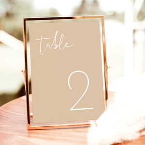 May include: A gold-framed table number sign with a beige background. The sign says "table 2" in white cursive font.