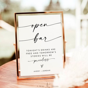 May include: A framed sign with the words "open bar" in elegant script. The sign also includes the text "Tonight's drinks are free and tomorrow's stories will be priceless" with a heart symbol and names "Avery + Jordan". The frame is gold.