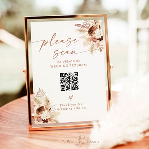 May include: A printable sign with a gold frame and a floral design. The sign says "Please Scan" to view our wedding program. A QR code is displayed below the text. The sign also says "Thank you for celebrating with us!" and "A Wild Bloom Printables".