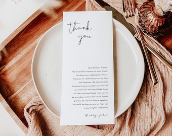 May include: A white thank you card with black calligraphy that reads "thank you". The card has a message expressing gratitude to family and friends for attending a wedding. The card is on a white plate with a brown wooden surface in the background.