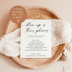 May include: A printable sign with the text "blow up their phones" in black cursive font. The sign is on a light brown wooden surface. The text below the title says "Text a photo or video to the bride or groom for them to reminisce the night!"  Some ideas are listed below: A photo of your table, a picture of their first dance, a candid photo of them laughing, a photo of toasts, speeches, a video of you or someone else dancing, a photo of cake cutting, a video of you sending love & good wishes. The names Avery and Jordan are listed below with phone numbers.