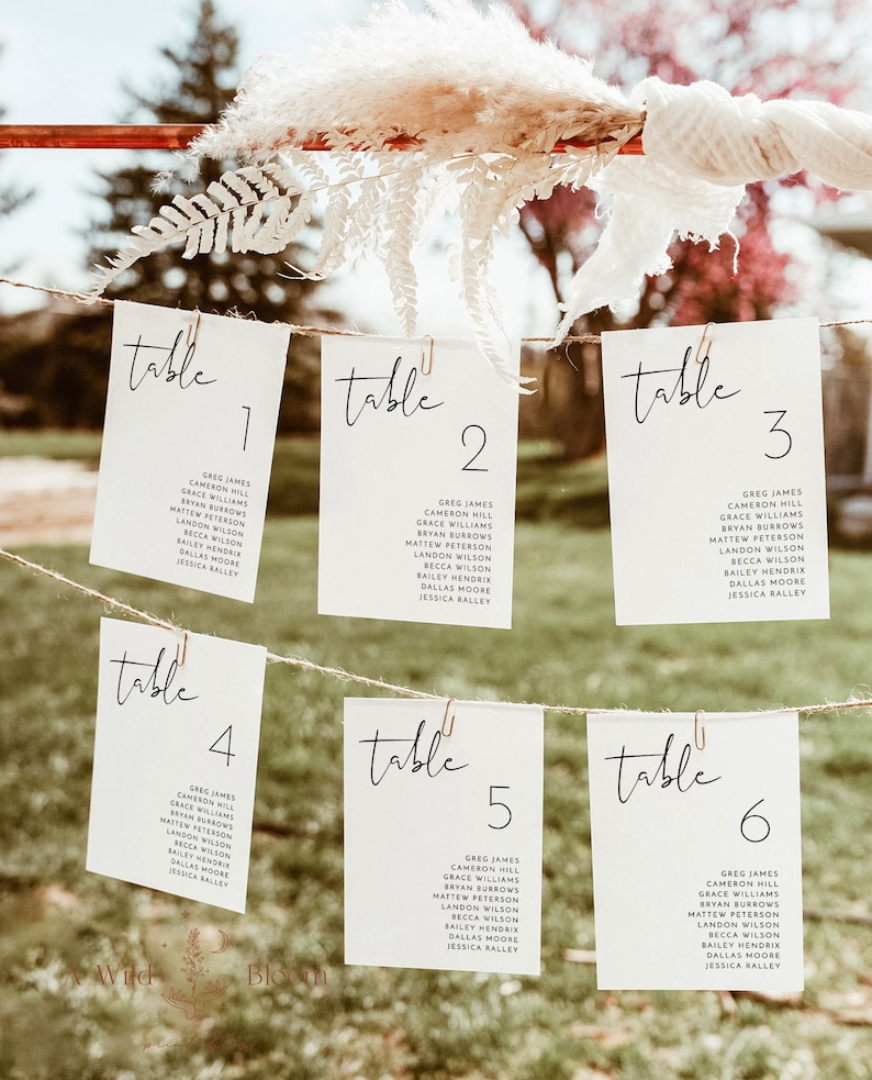 Pu&ograve; includere: Sei carte da tavolo bianche con scritta calligrafica nera che dice "tavolo" e un numero da 1 a 6. Le carte sono appese a una corda con delle clip.