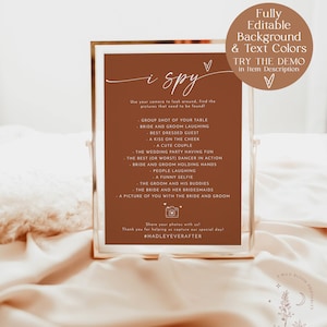 May include: A printable "I Spy" game card with a brown background and white text. The card lists items to find in wedding photos, such as "bride and groom laughing" and "a funny selfie". The card also includes the hashtag #HADLEYEVERAFTER.