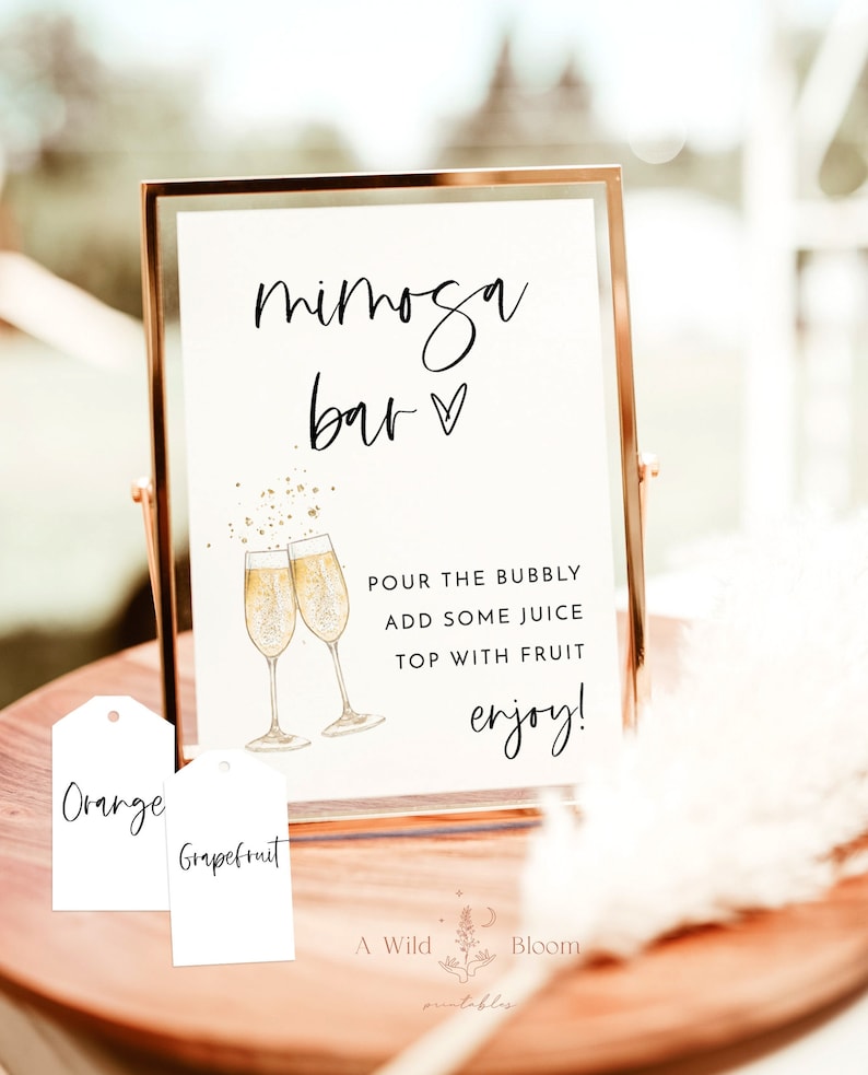 May include: A printable sign for a mimosa bar with the text "mimosa bar" and a heart. The sign also includes instructions for making mimosas: "Pour the bubbly, add some juice, top with fruit, enjoy!" There are two tags below the sign that say "Orange" and "Grapefruit".