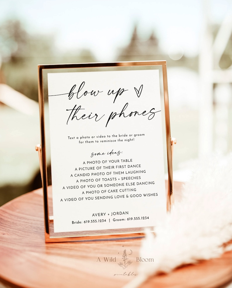 May include: A printable sign with the text "blow up their phones" in black script font. The sign instructs guests to text a photo or video to the bride and groom. It includes some ideas for photos and videos, such as a photo of their first dance, a candid photo of them laughing, and a video of them cutting the cake. The sign also includes the bride and groom's phone numbers.
