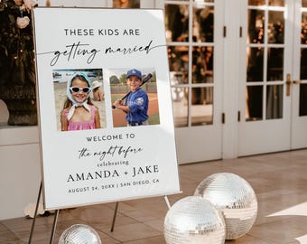 May include: White sign with black text that reads "These kids are getting married. Welcome to the night before celebrating Amanda + Jake. August 24, 20XX | San Diego, CA". Two photos are on the sign, one of a girl wearing a white hat and sunglasses and another of a boy wearing a baseball uniform. The sign is on a black easel.