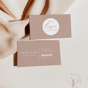 May include: A business card with the text "wild bloom creations PHOTOGRAPHY" and contact information, including a phone number, email address, website, and social media links. The card is light brown with white text. The background is a light brown fabric.