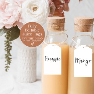 May include: Two glass bottles with cork tops filled with orange juice.  The bottles have white tags with black handwritten text that reads "Pineapple" and "Mango".  The bottles are sitting on a white surface with a white vase and pink flowers in the background.  The image includes a brown circle with the text "Fully Editable Juice Tags" and "Try the Demo in Item Description".