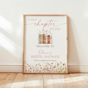 May include: A framed poster with the text "A New Chapter Begins" in a script font. The poster welcomes guests to Olivia's Bridal Shower. The design includes a stack of books and floral accents. The poster is 18x24 inches.