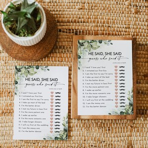 May include: Two "He Said, She Said" game cards with a botanical design. The cards have a list of statements with spaces for circling "one or both." One card is framed in wood. A small potted plant sits nearby.
