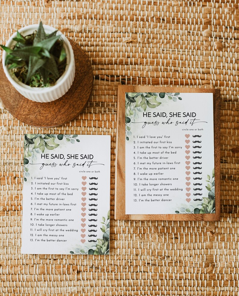 May include: Two "He Said, She Said" game cards with a botanical design. The cards have a list of statements with spaces for circling "one or both." One card is framed in wood. A small potted plant sits nearby.