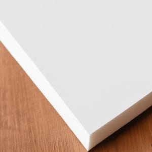 May include: A white foam board with a textured surface, shown at an angle. The board is on a wooden surface. The text "Foam Board" and "Zoomed in to show texture" is in the lower left corner.