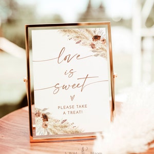 Może przedstawiać: Złoty znak z białym tłem i kwiatowym wzorem. Znak głosi "love is sweet" z sercem i "Please take a treat!"  Pod tekstem znajduje się logo "A Wild Bloom Printables".